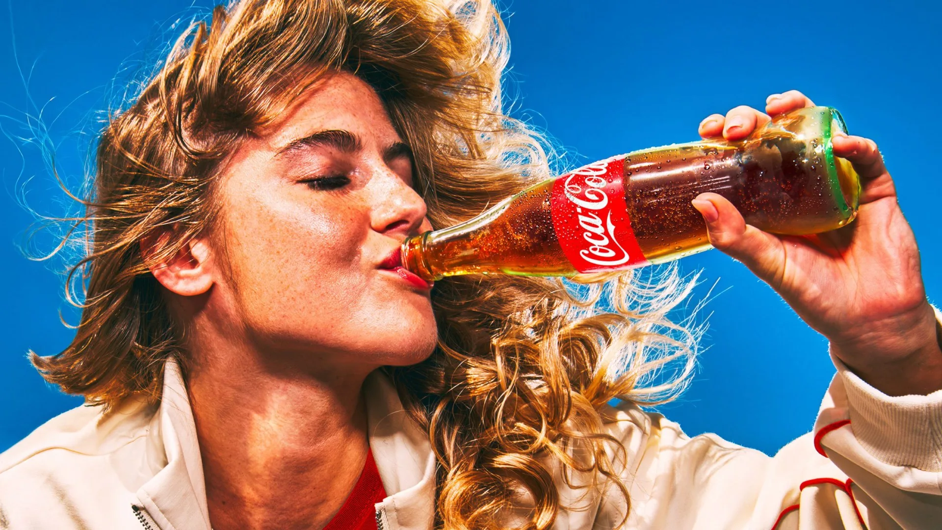 Fotografía publicitaria de una mujer bebiendo Coca-Cola en botella de vidrio.